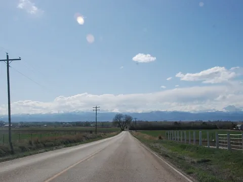 A county road on the northern Colorado plains running west toward the snow-covered Front Range in April