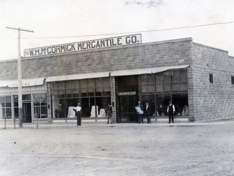 The W.H. McCormick Mercantile Co. at 1 N Parish Avenue in the early 1900s: a one-storey stone-block store with an awning, men standing along the unpaved street in front.