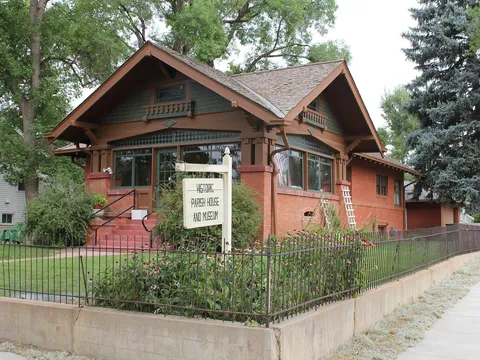 The 1914 Craftsman bungalow at 701 Charlotte Street behind its iron fence, with the Historic Parish House and Museum sign in the front garden